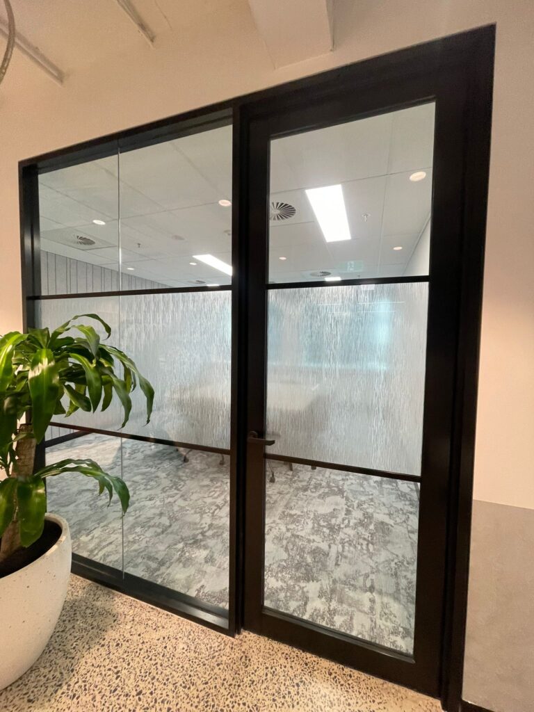 Office glass partition and door fitted with decorative architectural window film for privacy while maintaining natural light in a modern commercial workspace.