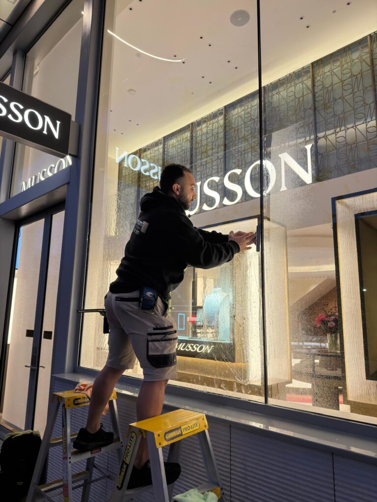 Installer applying 3M anti-graffiti window film to storefront glass